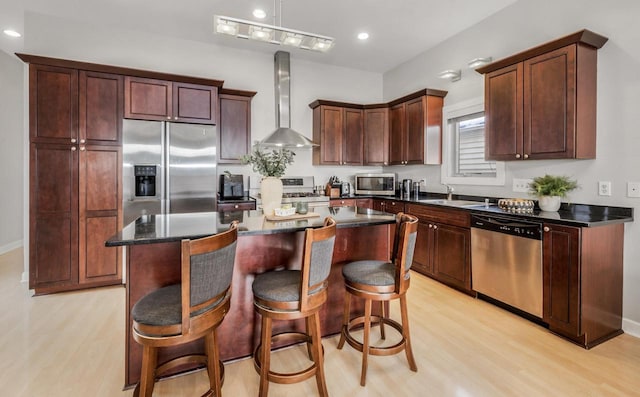 kitchen with a breakfast bar area, light wood finished floors, appliances with stainless steel finishes, a kitchen island, and wall chimney exhaust hood