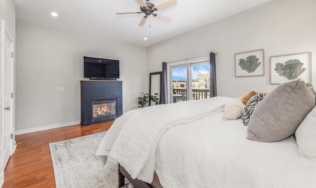 bedroom featuring recessed lighting, a fireplace, wood finished floors, baseboards, and access to exterior