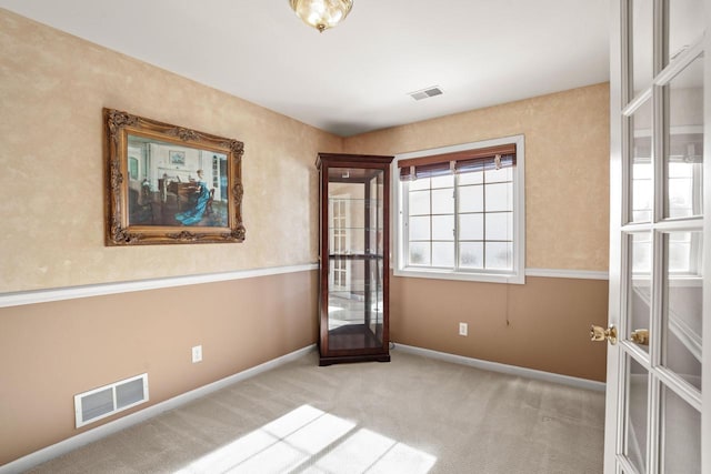 spare room with light colored carpet, french doors, visible vents, and baseboards