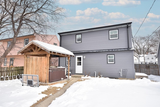 snow covered property with entry steps, fence, and a hot tub