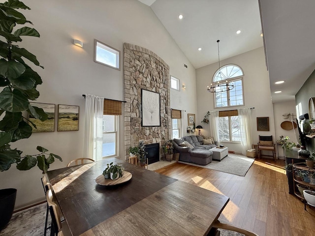 dining space with light wood-style floors, high vaulted ceiling, a stone fireplace, and an inviting chandelier