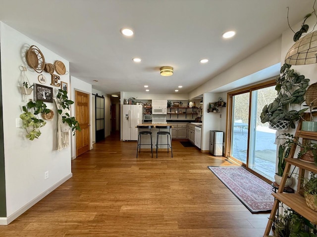 kitchen featuring a barn door, white appliances, a kitchen island, white cabinetry, and a kitchen breakfast bar