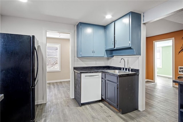 kitchen featuring dark countertops, freestanding refrigerator, white dishwasher, a sink, and blue cabinets