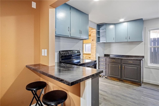 kitchen featuring a peninsula, a breakfast bar, light wood-style floors, black electric range oven, and dark countertops