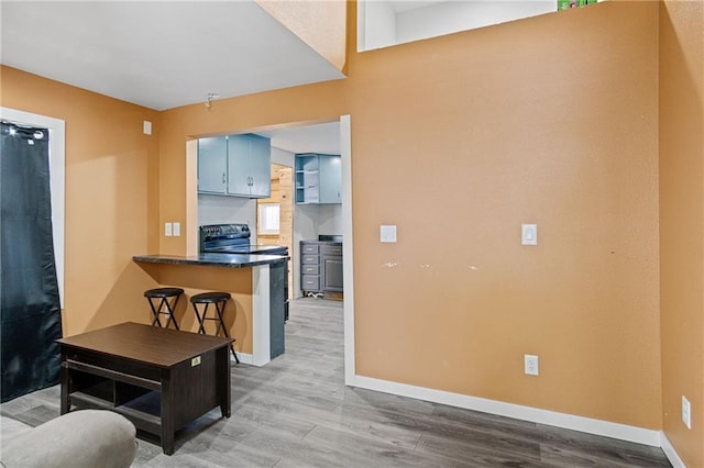 kitchen featuring blue cabinets, a peninsula, wood finished floors, baseboards, and dark countertops