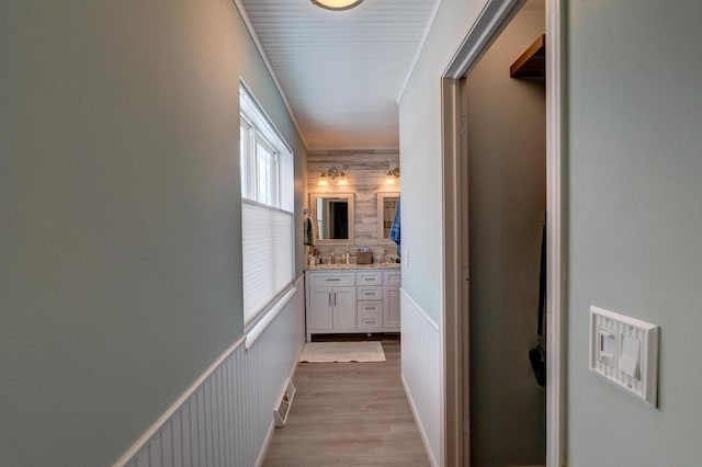 corridor with light wood-type flooring, visible vents, ornamental molding, and wainscoting