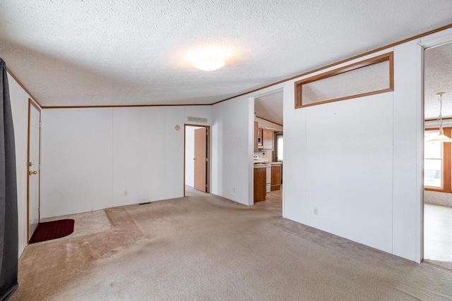 empty room featuring light carpet, ornamental molding, vaulted ceiling, and a textured ceiling