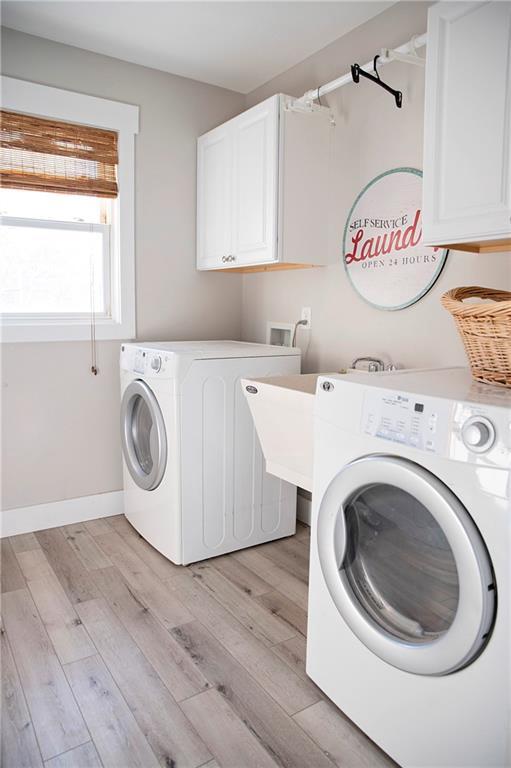 laundry room with light wood-type flooring, washing machine and clothes dryer, cabinet space, and baseboards