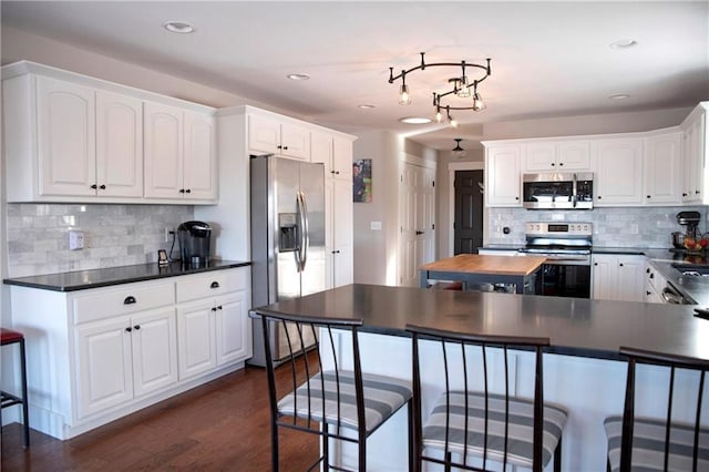 kitchen with dark wood-style flooring, white cabinetry, appliances with stainless steel finishes, decorative backsplash, and dark countertops