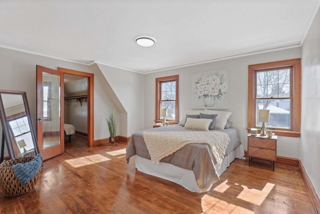 bedroom with light wood-type flooring, baseboards, a walk in closet, and ornamental molding