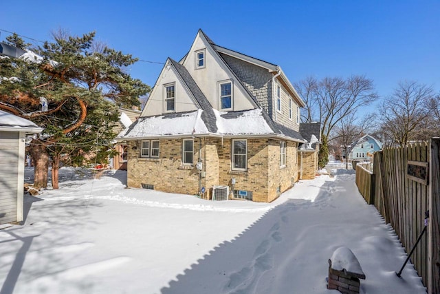 view of snowy exterior with central AC unit, brick siding, fence, and stucco siding