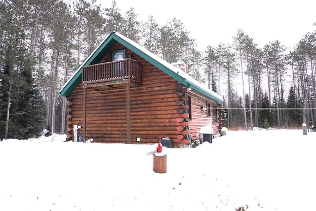 snow covered property with log exterior and a balcony