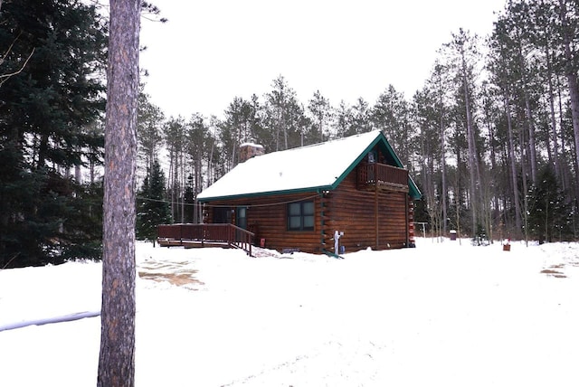 snow covered property with log exterior, a chimney, and a wooden deck