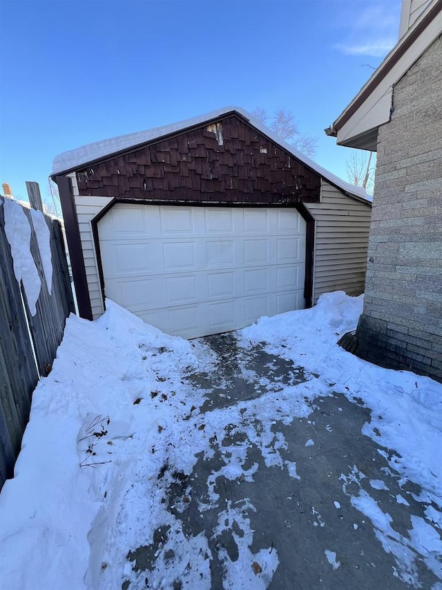 snowy yard featuring a garage, an outbuilding, and fence