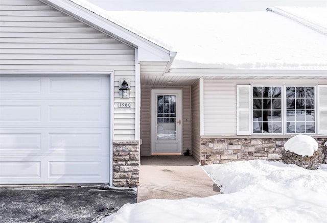 snow covered property entrance with a garage and stone siding