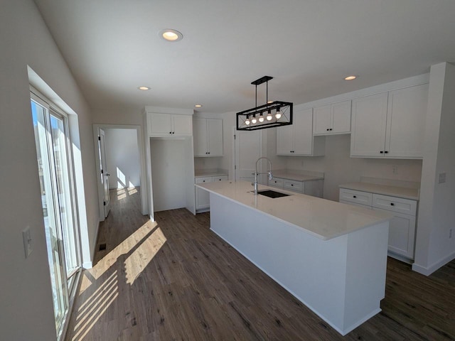 kitchen with decorative light fixtures, a center island with sink, light countertops, white cabinets, and a sink