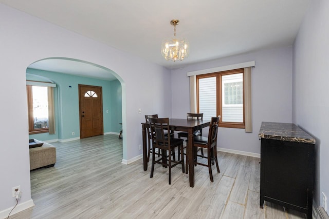 dining space with light wood-type flooring, an inviting chandelier, baseboards, and arched walkways