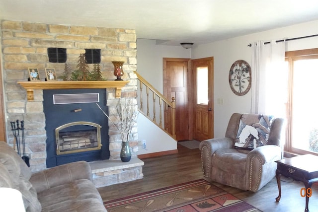 living area with a stone fireplace, plenty of natural light, wood finished floors, and visible vents