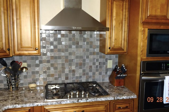 kitchen featuring wall oven, brown cabinetry, wall chimney exhaust hood, built in microwave, and stainless steel gas cooktop