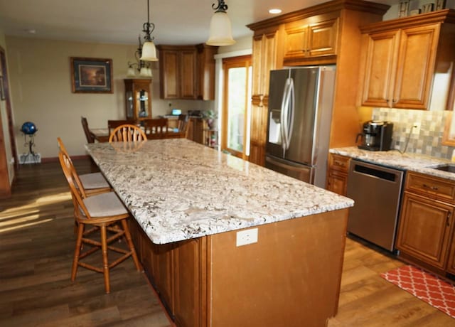 kitchen featuring brown cabinets, decorative light fixtures, stainless steel appliances, a kitchen island, and wood finished floors