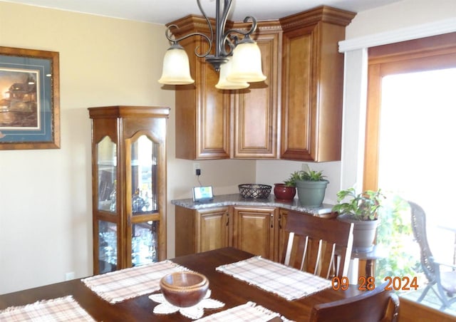 kitchen with brown cabinetry, hanging light fixtures, and light stone counters