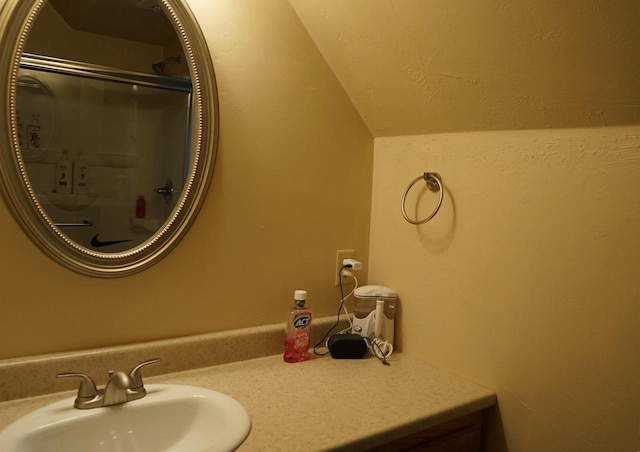 bathroom with lofted ceiling, a textured wall, and vanity