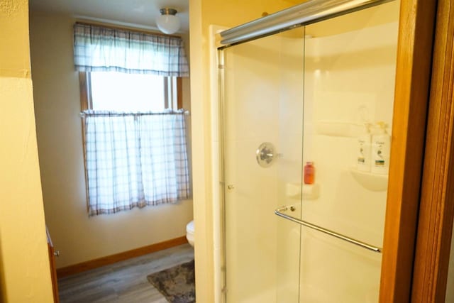 full bathroom with toilet, a stall shower, baseboards, and wood finished floors