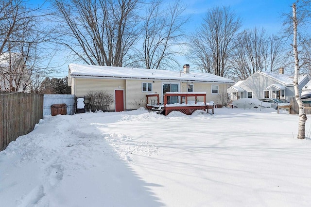 snow covered back of property featuring a deck and fence