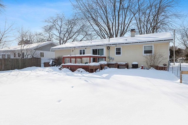 snow covered back of property featuring a chimney, fence, and a wooden deck