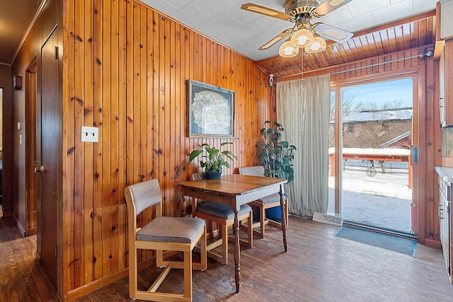 dining space featuring a ceiling fan, wooden walls, and wood finished floors