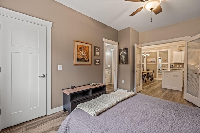 bedroom featuring ensuite bathroom, ceiling fan with notable chandelier, baseboards, and light wood-style floors