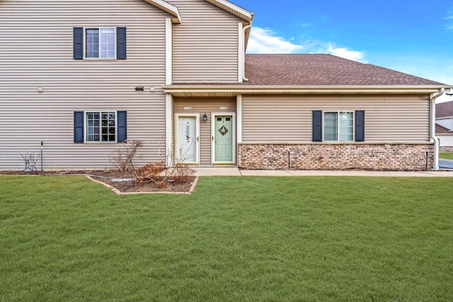 view of front facade featuring a front yard, roof with shingles, and brick siding