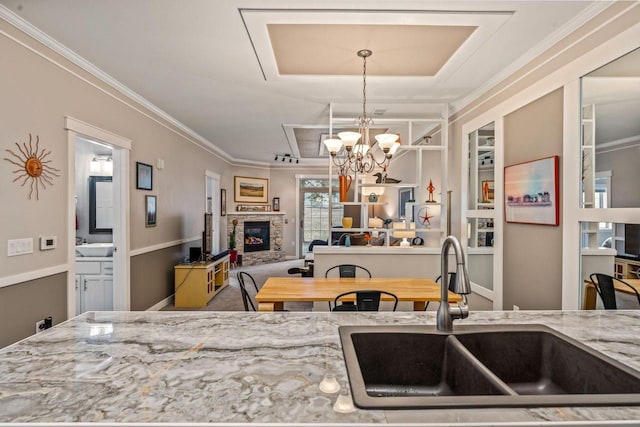 kitchen featuring ornamental molding, light stone counters, open floor plan, a fireplace, and a sink