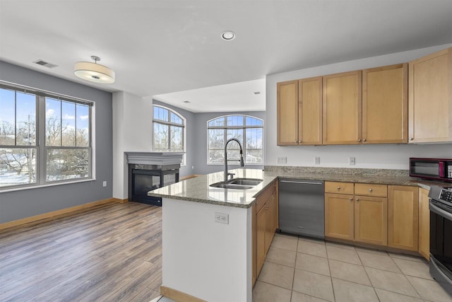 kitchen featuring a sink, light stone countertops, dishwasher, a peninsula, and a multi sided fireplace