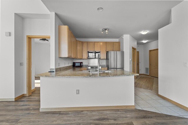 kitchen with black microwave, a peninsula, visible vents, freestanding refrigerator, and light stone countertops