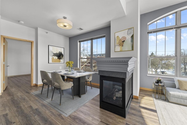 dining space featuring baseboards, visible vents, wood finished floors, and a multi sided fireplace