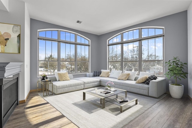 living area featuring light wood-type flooring, a fireplace, visible vents, and baseboards