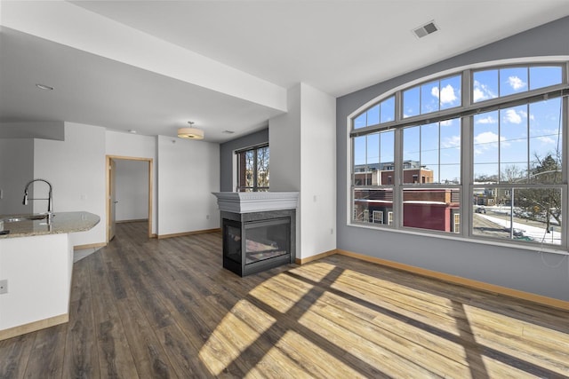 unfurnished living room with dark wood finished floors, visible vents, a multi sided fireplace, a sink, and baseboards