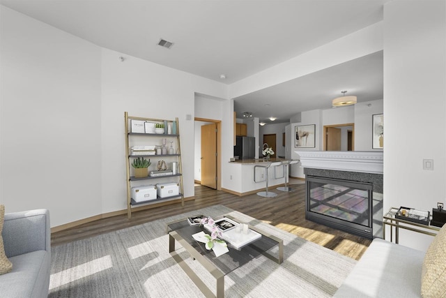 living room featuring baseboards, visible vents, dark wood finished floors, and a glass covered fireplace