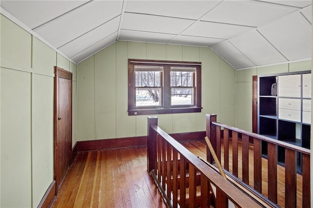 hall with lofted ceiling, a decorative wall, wood finished floors, and an upstairs landing