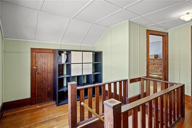 hall featuring a paneled ceiling, a decorative wall, wood finished floors, an upstairs landing, and vaulted ceiling