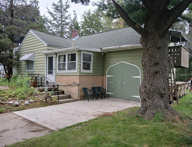 back of property with a patio area, roof with shingles, a chimney, and brick siding