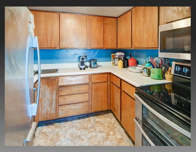 kitchen featuring light countertops, stone finish flooring, brown cabinetry, and stainless steel appliances