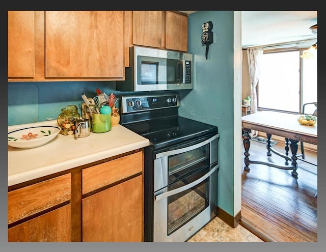 kitchen with baseboards, brown cabinets, appliances with stainless steel finishes, and light countertops