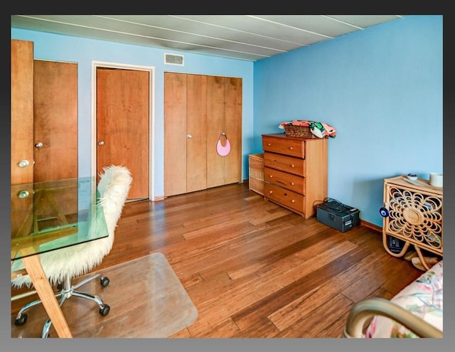 bedroom with visible vents, multiple closets, and wood finished floors