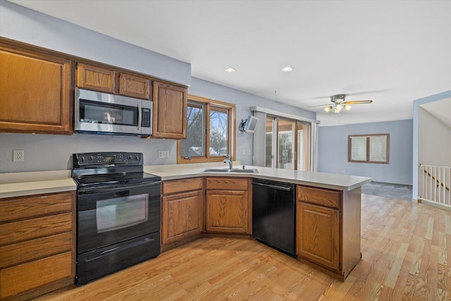 kitchen with a peninsula, a sink, light countertops, black appliances, and brown cabinetry