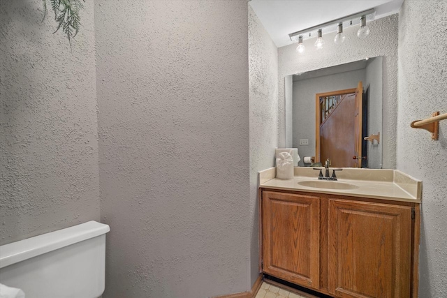 half bath with a textured wall, vanity, and toilet