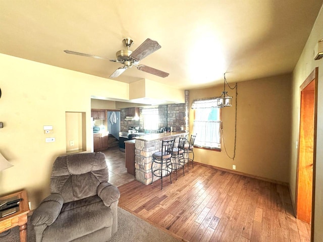 kitchen with ceiling fan, a breakfast bar area, open floor plan, wood finished floors, and a peninsula