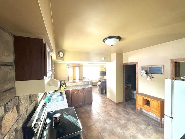 kitchen featuring a peninsula, stainless steel electric stove, a sink, and freestanding refrigerator