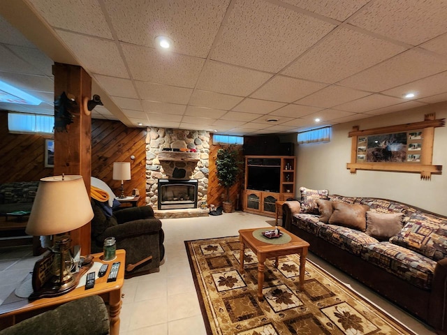 living area with a paneled ceiling, wood walls, and a stone fireplace